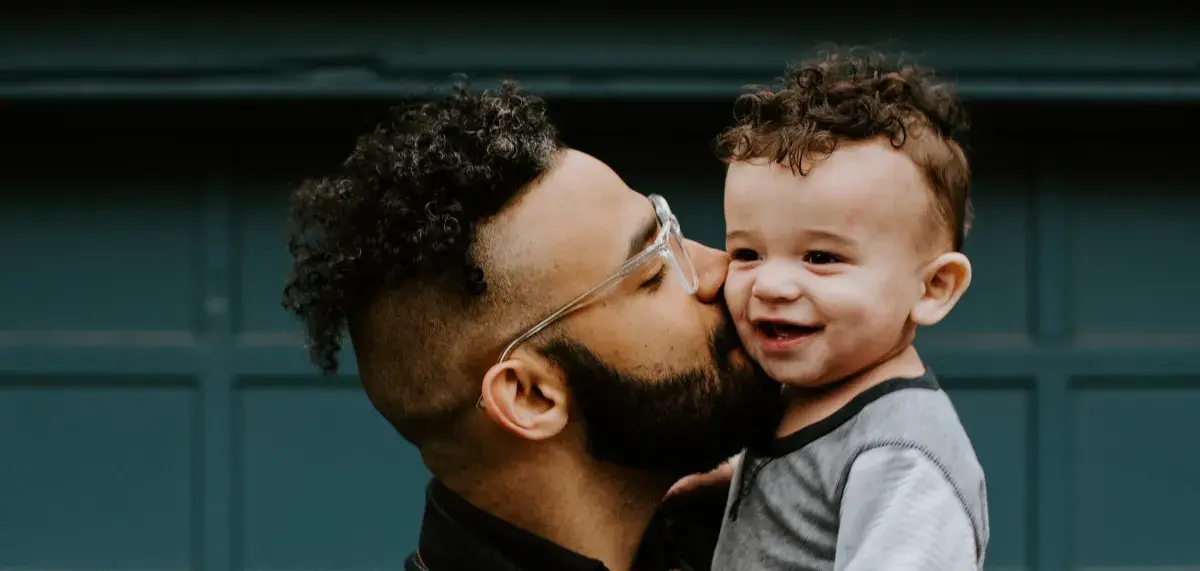 Adult holding a child up and giving them a kiss on the cheek.