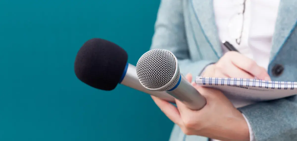 Hand holding two microphones and writing in a notebook