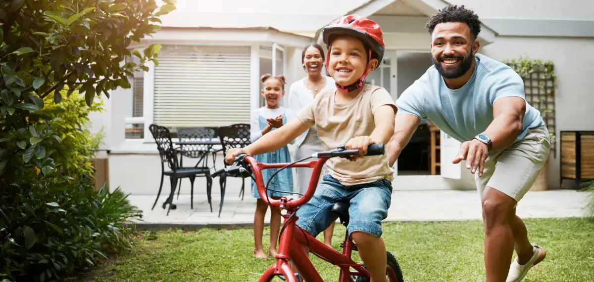 Child rides a bike for the first time as father stands behind smiling