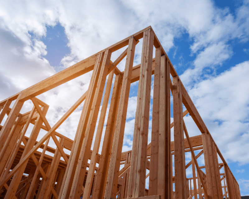 A building is being built in the foreground, in the background is a sunny sky.