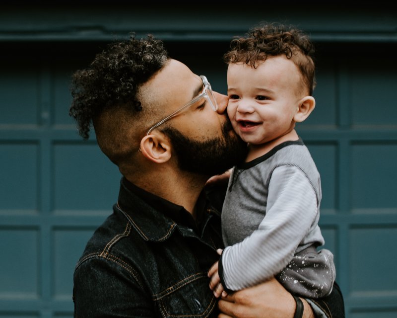 Adult holding a child up and giving them a kiss on the cheek.
