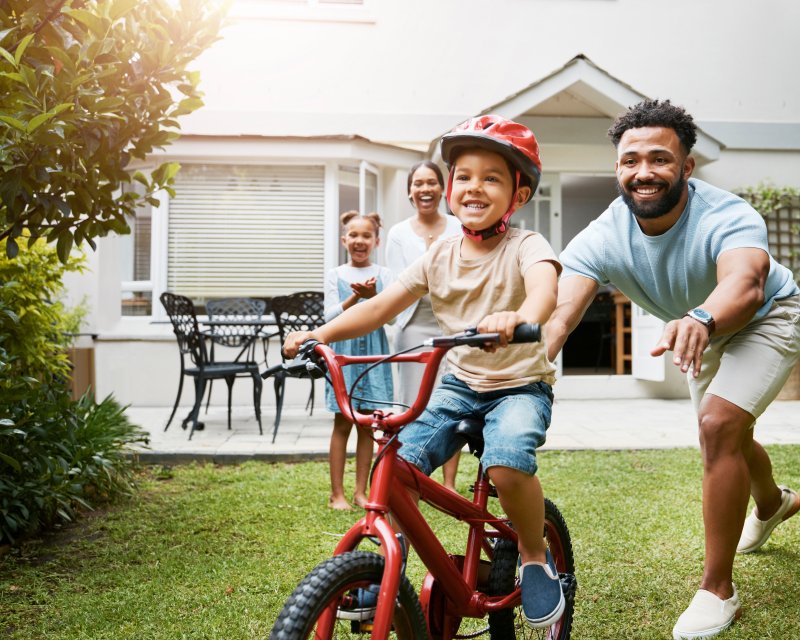 Child rides a bike for the first time as father stands behind smiling