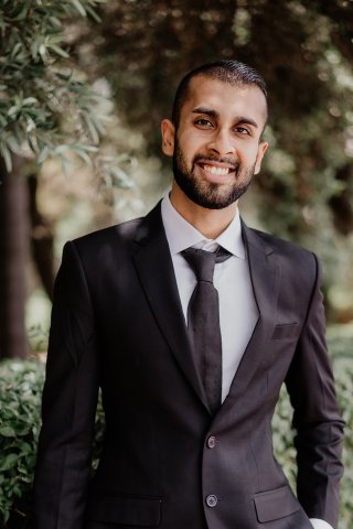 Samir Goel smiles in a suit and tie with trees in the background