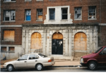 Exterior of Meridian Manor apartments before renovations. Boards in windows.
